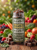 A jar of Happy Soul Fruits & Veggies gummies stands on a wooden table surrounded by fresh fruits, vegetables, and loose gummy cubes, with a blurred garden background.